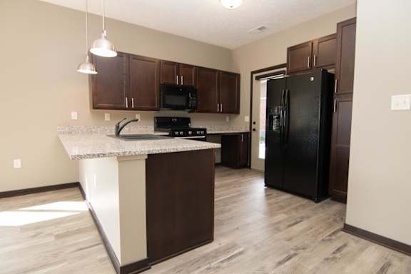 A kitchen with a black refrigerator and brown cabinets.