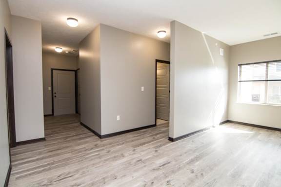 A spacious living room with light brown flooring and white walls.