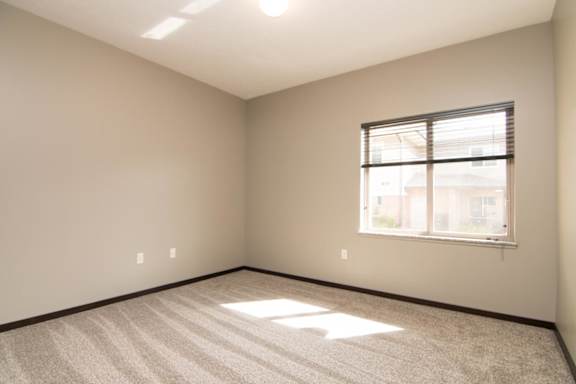A room with a carpeted floor and a window with blinds.