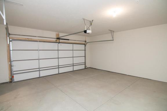A large empty garage with a white door and a grey floor.