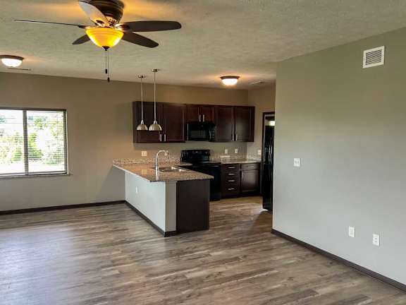 a kitchen with a dark wooden cabinets, granite countertops, hardwood flooring, and two pendant lights