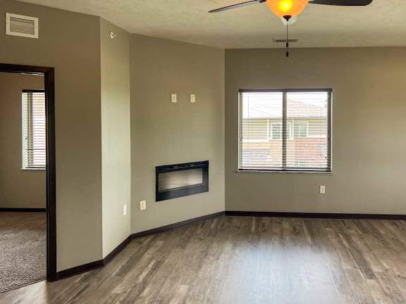 a living room with a fireplace, a large window, a door to the den, and a ceiling fan