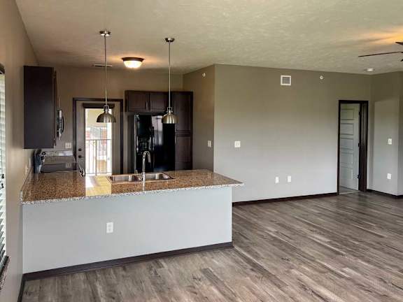 a kitchen with a dark wooden cabinets, granite countertops, hardwood flooring, and two pendant lights