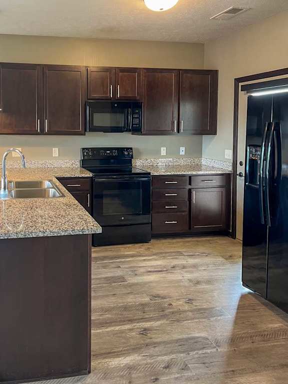a kitchen with dark wood cabinets, granite countertops, and black appliances