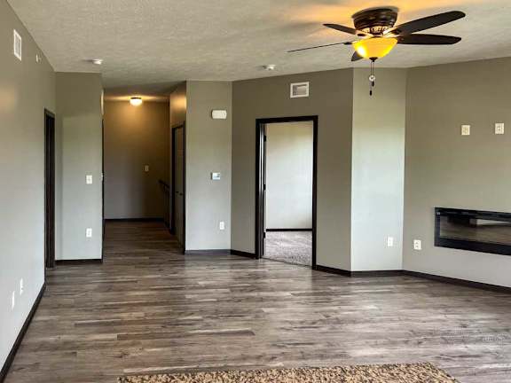 a living room with hard wood flooring, a fireplace, a ceiling fan, and a door to the den space