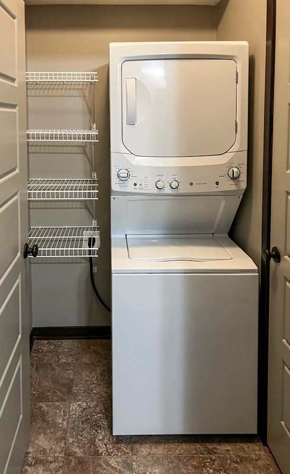 a stackable washer and dryer in a laundry room attached to the bathroom with built-in shelving