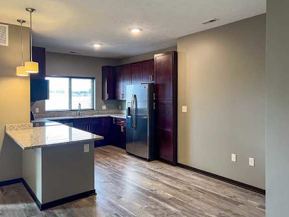 a kitchen with warm wooden cabinets, granite countertops, hardwood flooring, and stainless steel appliances