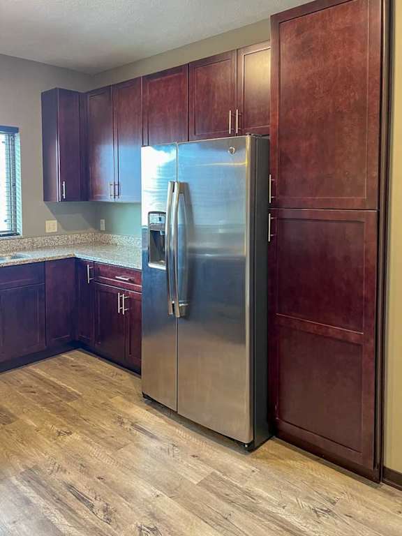 a kitchen with warm wooden cabinets, granite countertops, hardwood flooring, and stainless steel appliances