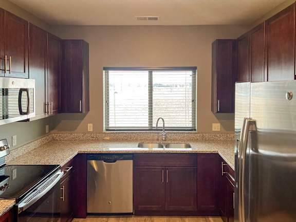 a kitchen with warm wooden cabinets, granite countertops, hardwood flooring, and stainless steel appliances