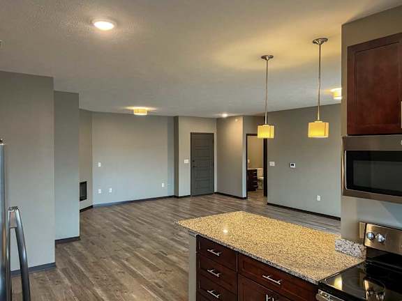 a kitchen with a granite peninsula countertop in front of a living room with hardwood flooring