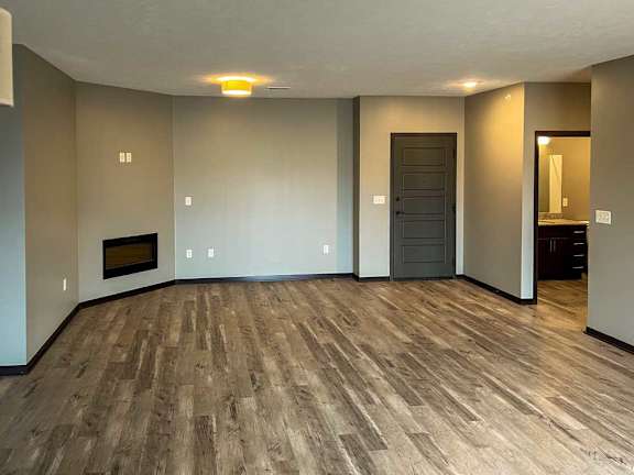 a living room with hardwood flooring, a fireplace, and a hallway with a door to the bathroom