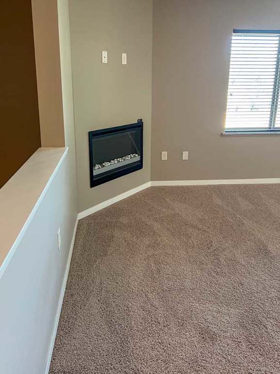 a living room with carpeted flooring, several windows, a ceiling fan, and a fireplace