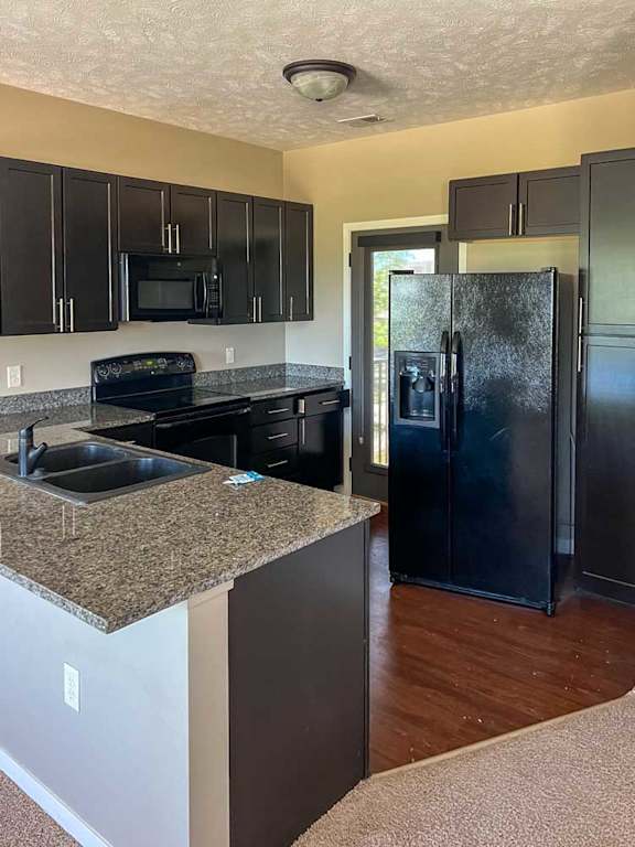 a kitchen with dark wooden cabinets, granite countertops, hardwood flooring, and black appliances