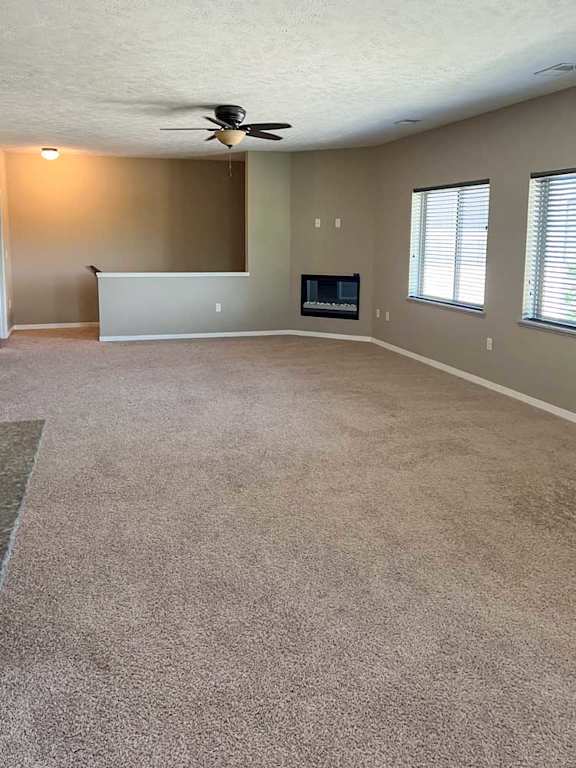 a living room with carpeted flooring, several windows, a ceiling fan, and a fireplace