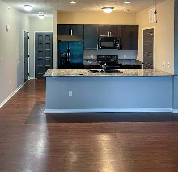 a kitchen with dark wooden cabinets, granite countertops, and black appliances