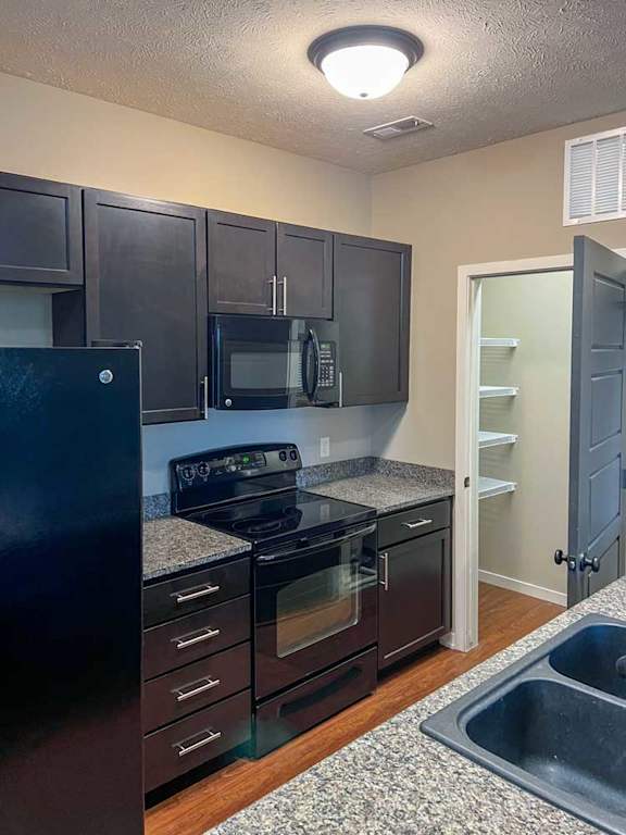 a kitchen with dark wooden cabinets, granite countertops, and black appliances