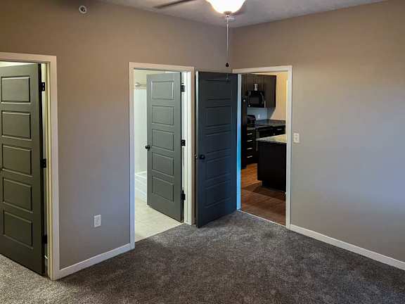 a bedroom with carpeted flooring, a walk-in closet, an attached bathroom, and a ceiling fan