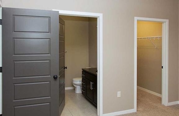 a bedroom with carpeted flooring, and an attached bathroom and walk-in closet