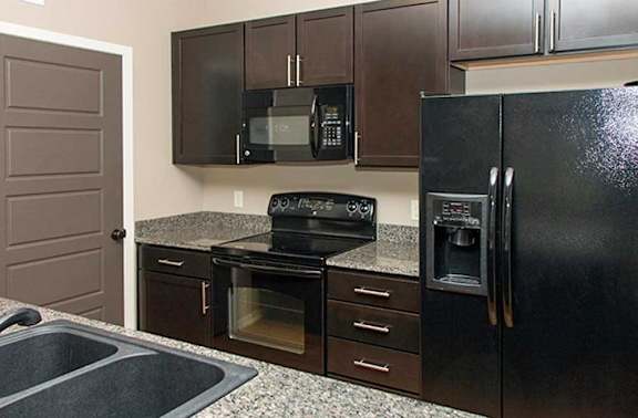 a kitchen with dark wooden cabinets, granite countertops, and black appliances