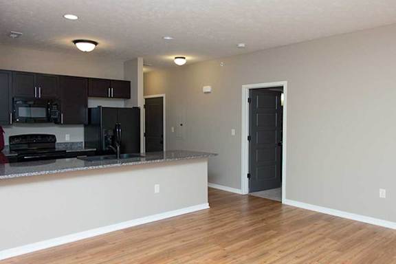 a kitchen with dark wooden cabinets, granite countertops, hardwood flooring, and black appliances