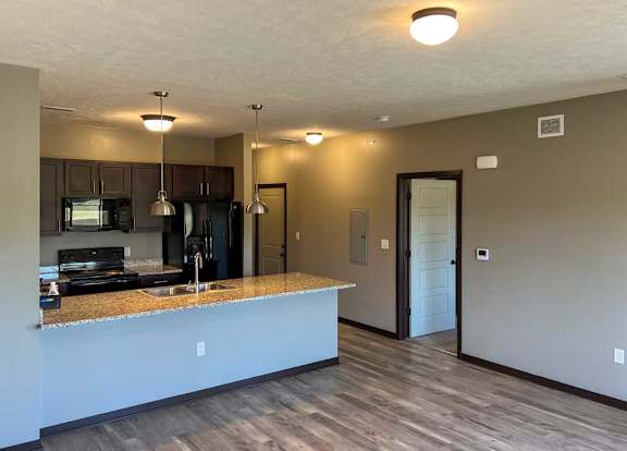 a kitchen with dark wooden cabinets, granite countertops, and black appliances featuring a large peninsula countertop