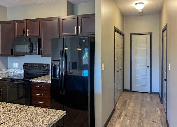 a kitchen with dark wooden cabinets, granite countertops, and black appliances in front of a hallway to the attached garage