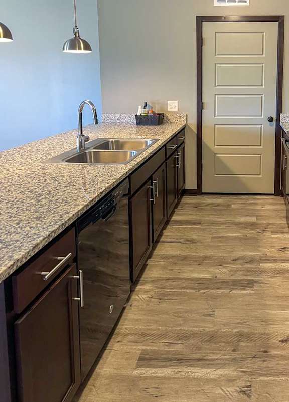 a kitchen with dark wooden cabinets, granite countertops, hardwood flooring, and black appliances