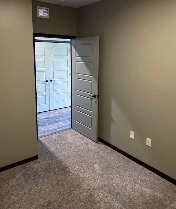 a den with carpeted flooring and a door leading to the front entry hallway