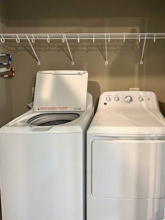 a full-sized side-by-side washer and dryer in a closet with overhead shelf storage