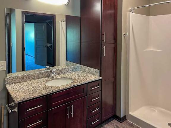 a bathroom with a granite vanity sink, mirror, tall storage cabinet, and walk-in shower
