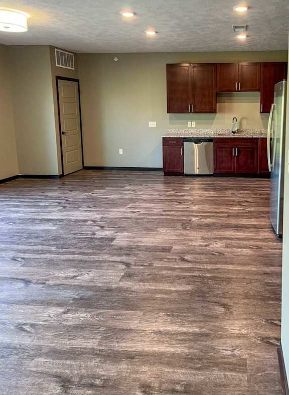 an open-concept living room and kitchen with red-brown cabinets and hard wood flooring