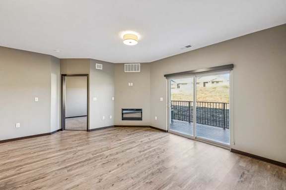 A spacious room with wooden flooring and a sliding glass door leading to a balcony.