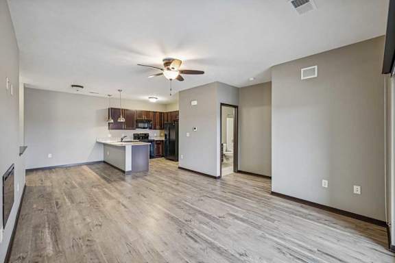 A spacious room with a ceiling fan and a kitchen area in the background.