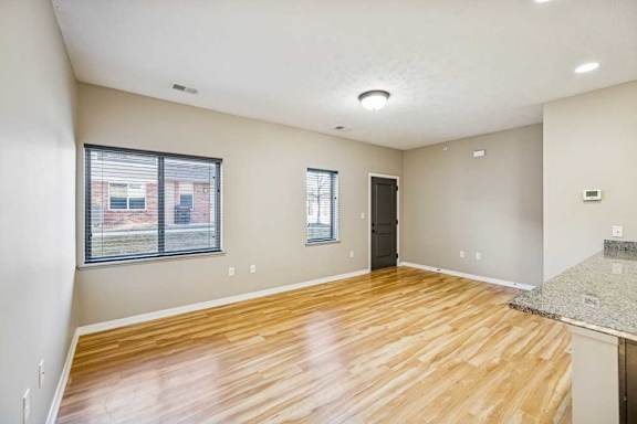 A large living room with wooden floors and large windows. The front door is dark and on the right.