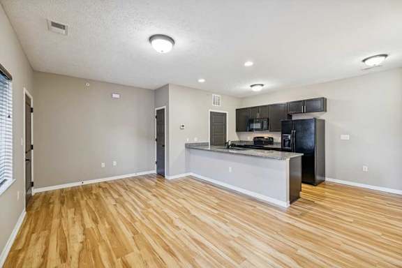 An apartment kitchen with wooden floors, black appliances, and granite countertops..