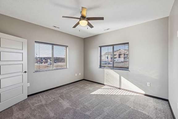 A room with a ceiling fan and two windows.
