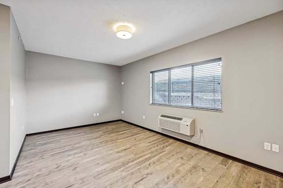 A room with a window, air conditioner, and wooden flooring.