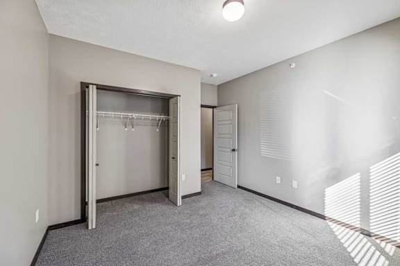 A room with a grey carpet and a white wall with a door and a window.