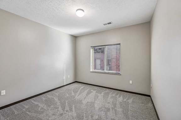 A room with a window and a grey carpet.