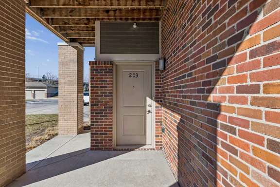 A white door with the number 203 on it is in a brick wall.