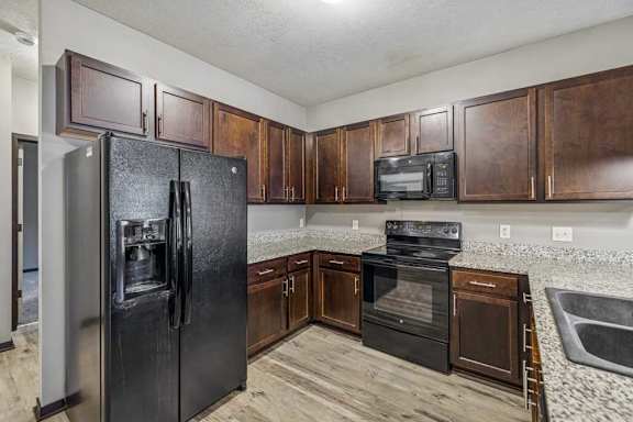 A kitchen with a black refrigerator and brown cabinets.