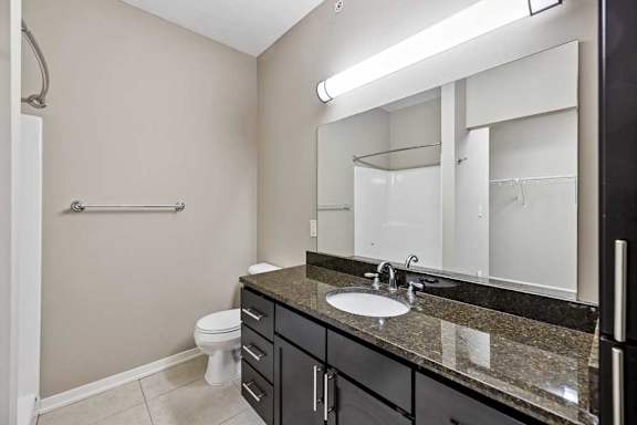 A bathroom with a granite vanity, dark wooden cabinets, and an oversized mirror with overhead lighting.
