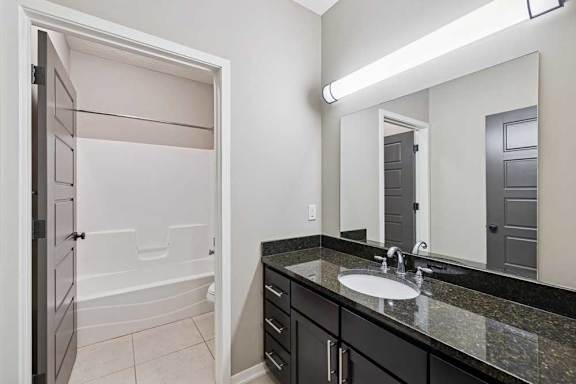 A bathroom with a wide granite vanity sink, oversized mirror, and door to private lavatory and wash room.
