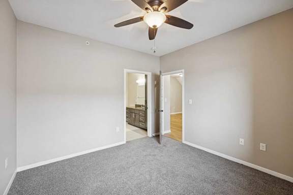 A carpeted bedroom with a ceiling fan, and an ensuite bathroom and walk-in closet.