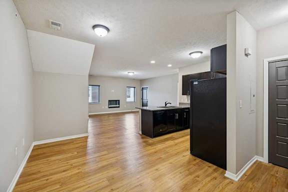 A dining room open to a kitchen with dark cabinets, in front of a spacious living room.