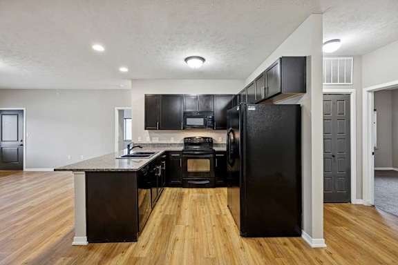 A kitchen with dark wooden cabinets, granite countertops, black appliances, and a peninsula countertop.