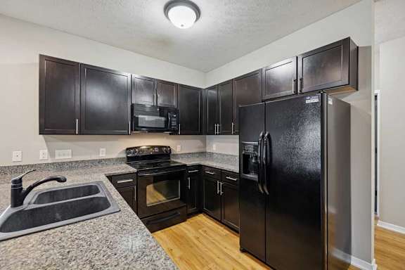 A kitchen with dark wooden cabinets, granite countertops, and black-finish appliances.