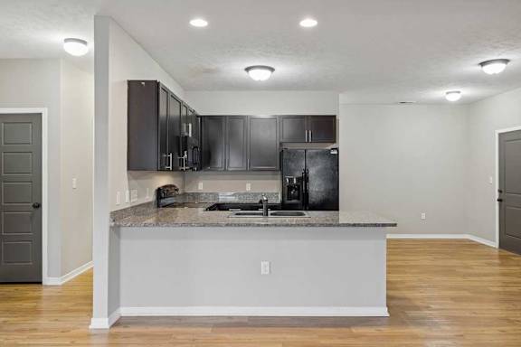 A kitchen with dark wooden cabinets, granite countertops, black appliances, and a peninsula countertop.