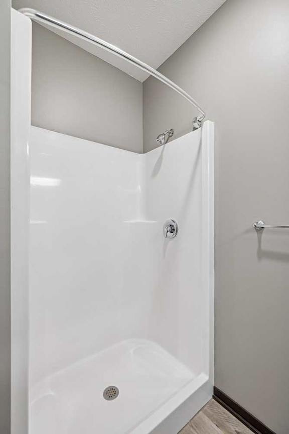 A white shower stall with a door and a drain.