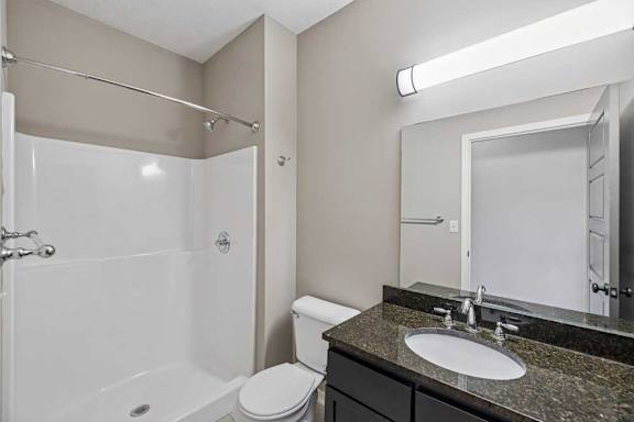 A bathroom with a granite vanity, large mirror, and a walk-in shower.